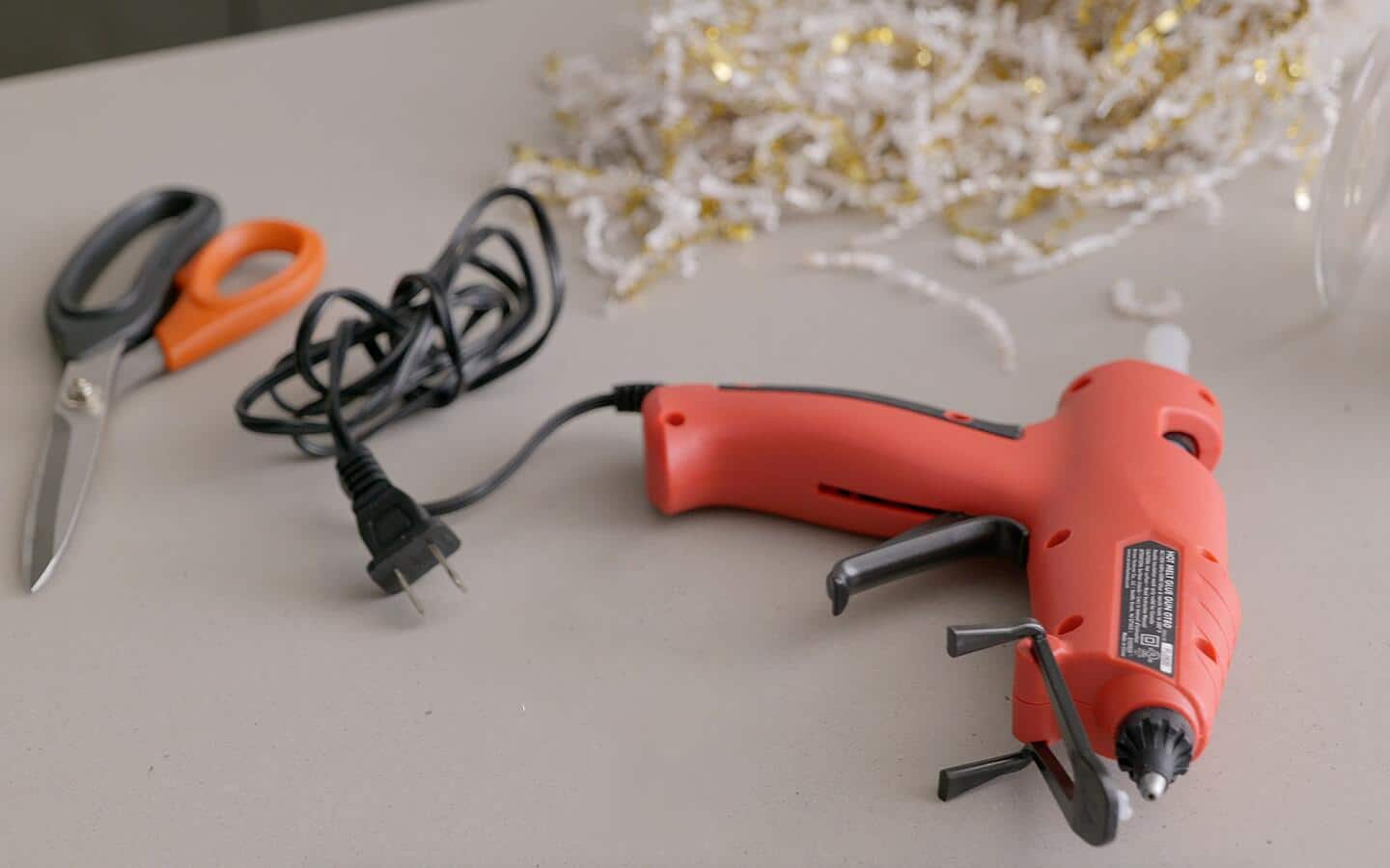 Shredded paper, a glue gun and a pair of scissors sit on a counter. 