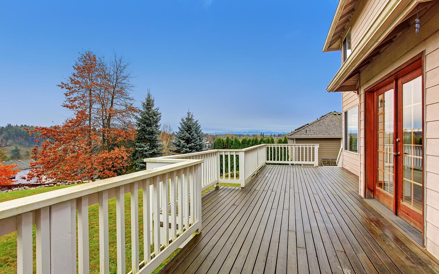 Double doors lead out to a wraparound wooden deck with a white railing. Double doors lead out to a wraparound wooden deck with a white railing.