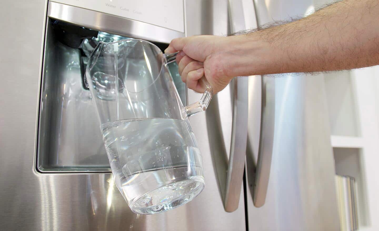 A person fills a pitcher with water from a refrigerator water dispenser.