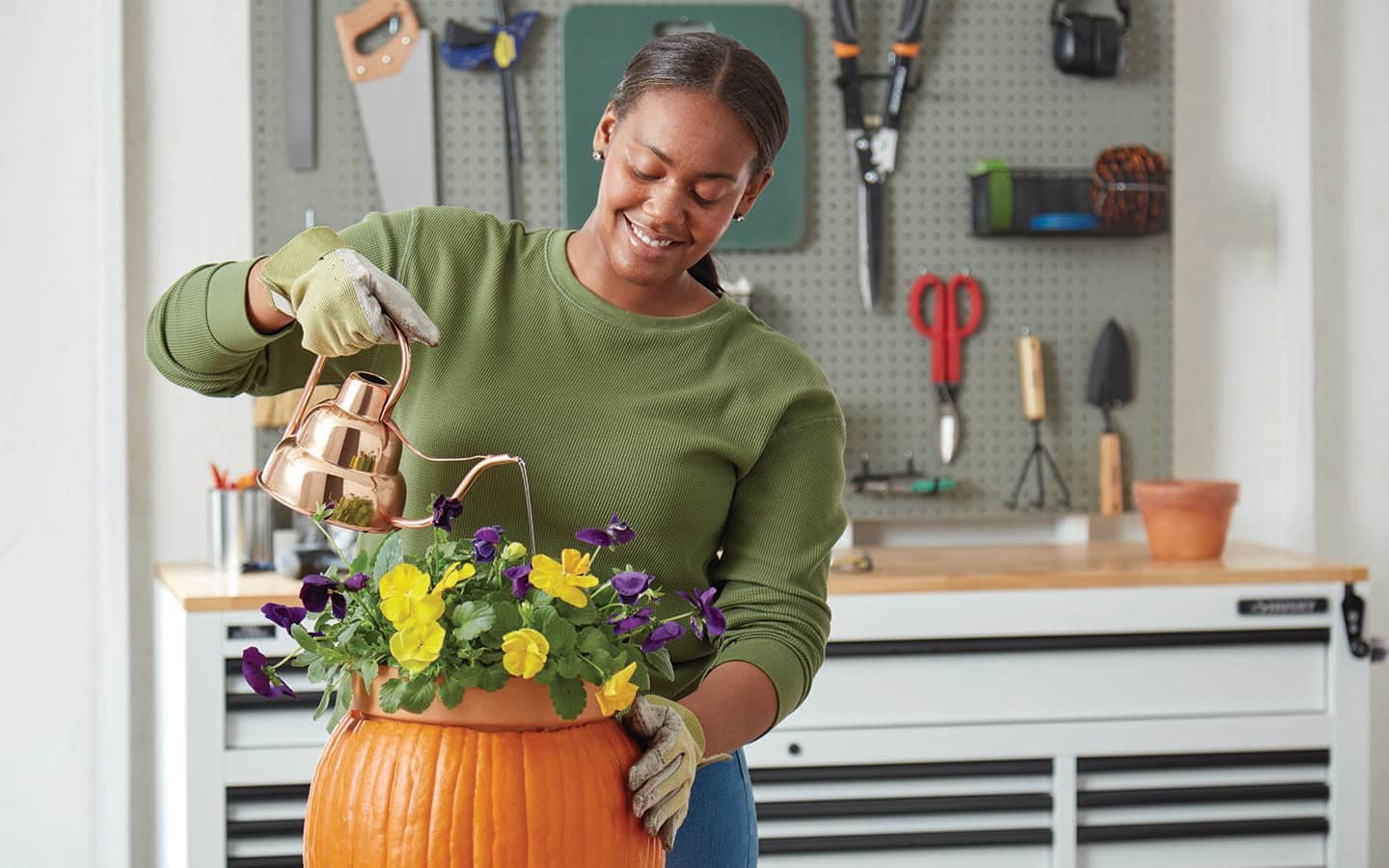 Person using a watering can to pour water into a pot of pansies inserted in a fresh pumpkin Person using a watering can to pour water into a pot of pansies inserted in a fresh pumpkin