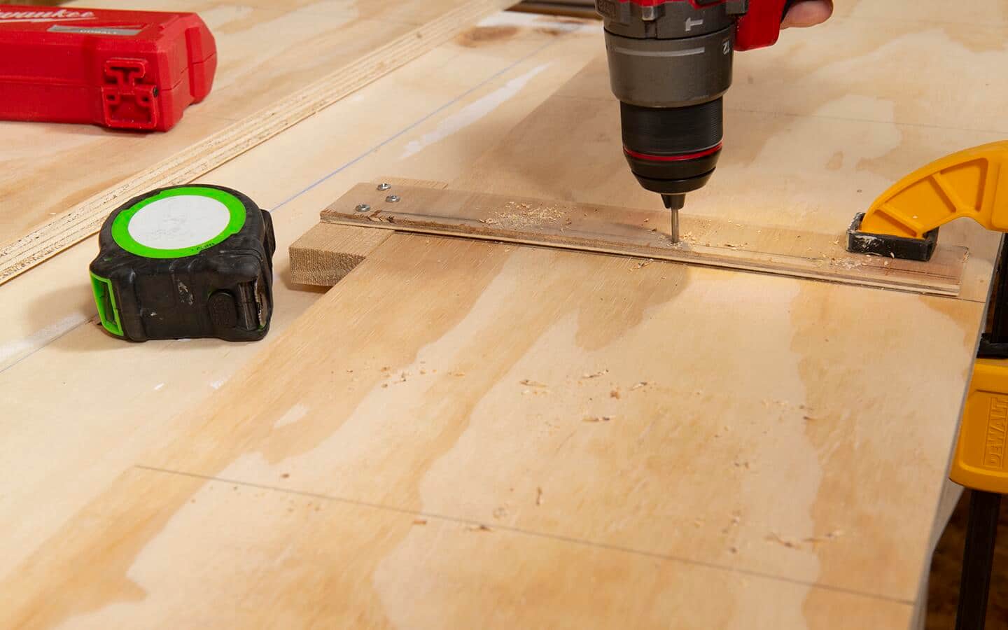 A jig is used to locate pilot holes in a piece of plywood that will be the upright side of a shelving unit.