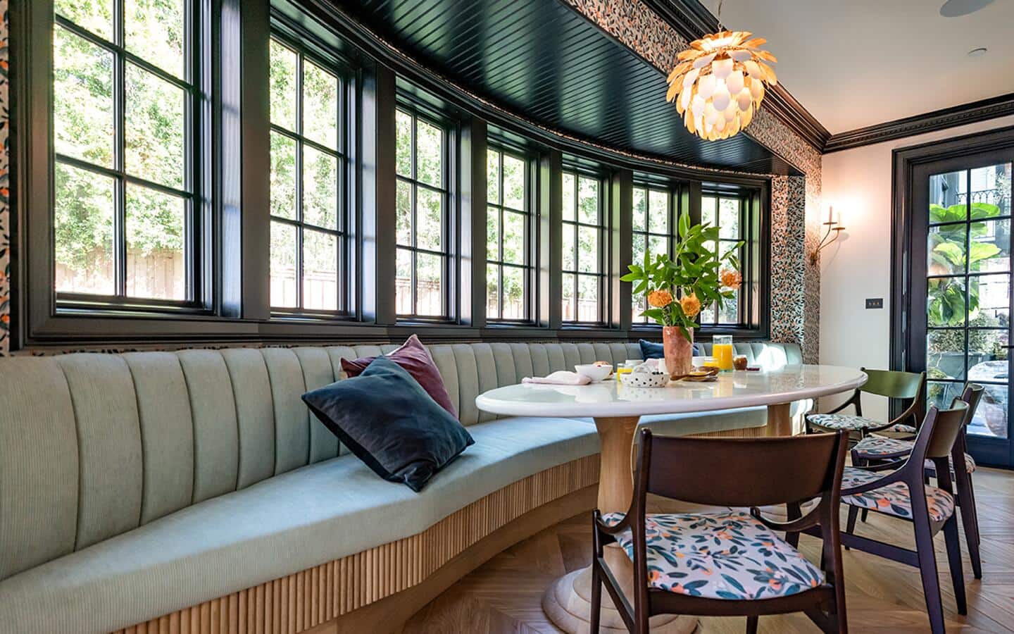 A kitchen with booth seating, table and chairs in front of a row of matching windows.
