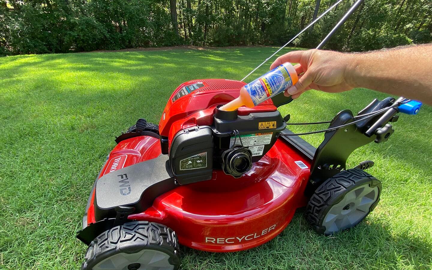 A person pours fuel cleaner into a lawn mower engine. A person pours fuel cleaner into a lawn mower engine.