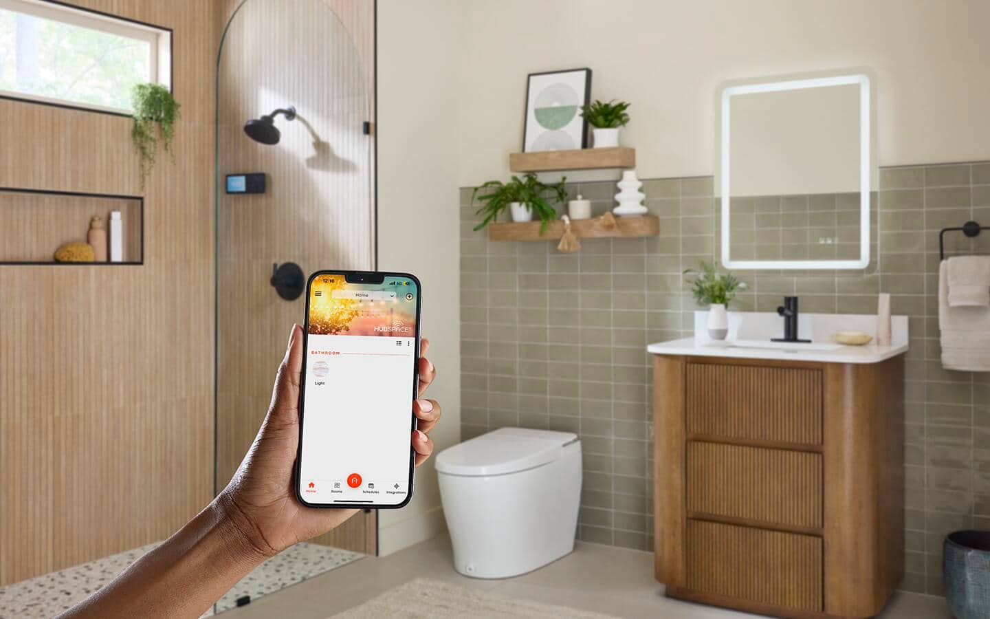 A person holding a phone displaying an app that controls the smart tech visible in the background of a bathroom.
