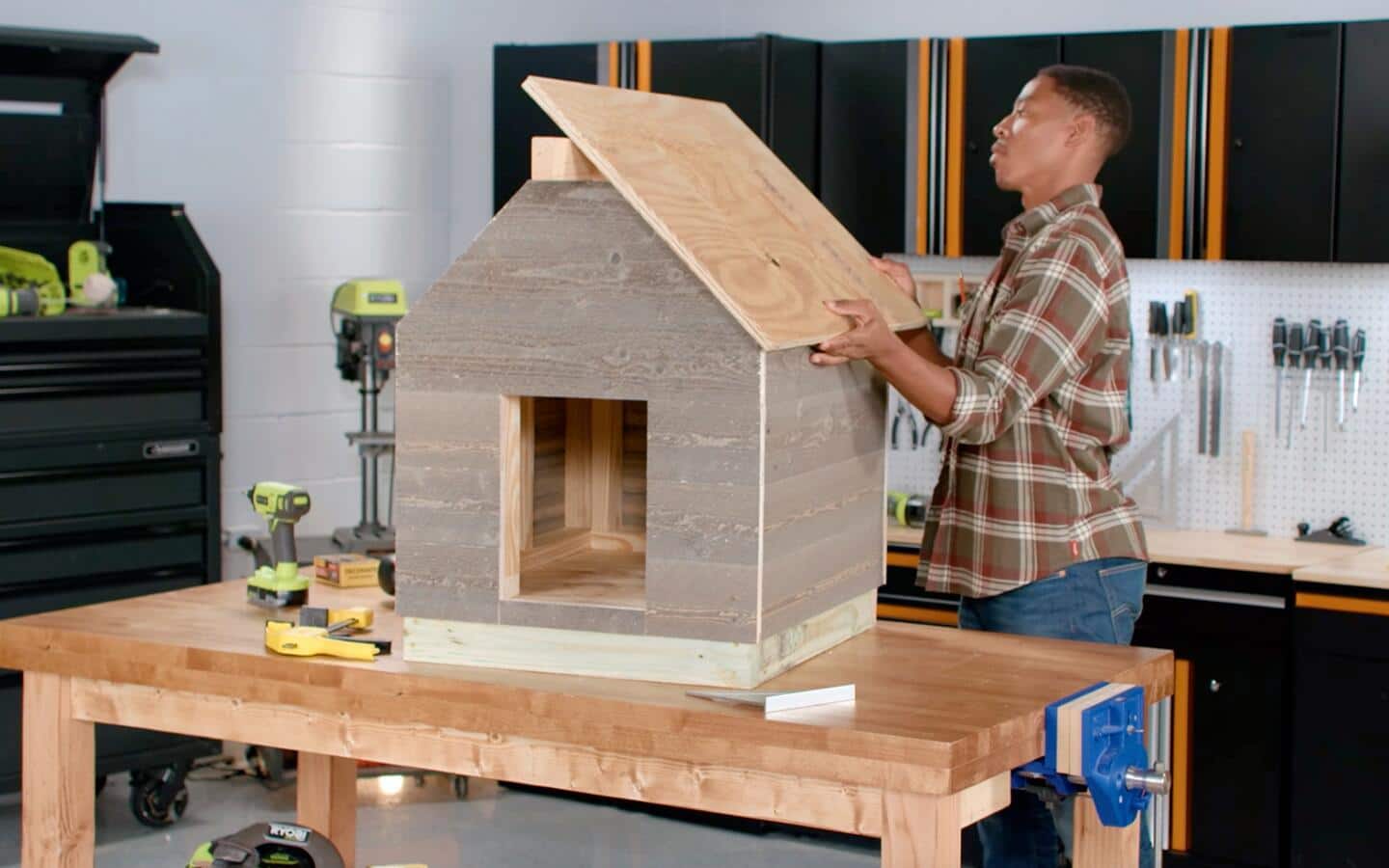 A person installing plywood to form a dog house's roof.