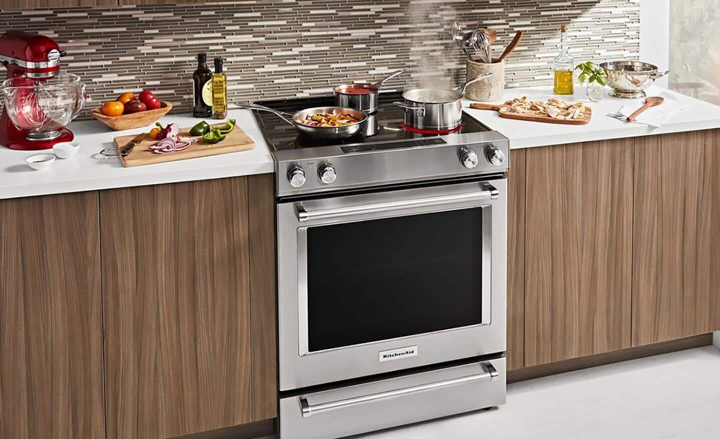 A convection oven sits in a kitchen surrounded by food preparation on countertops. It is the size of a conventional oven, and it has a stovetop with food being cooked on it.