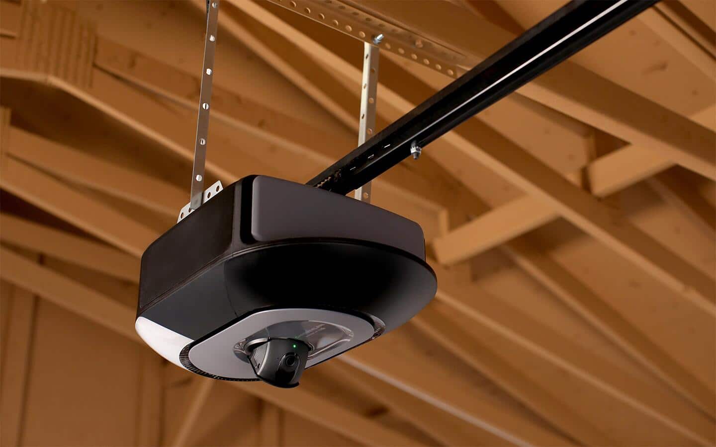 A smart garage door opener hangs from the ceiling of a garage.