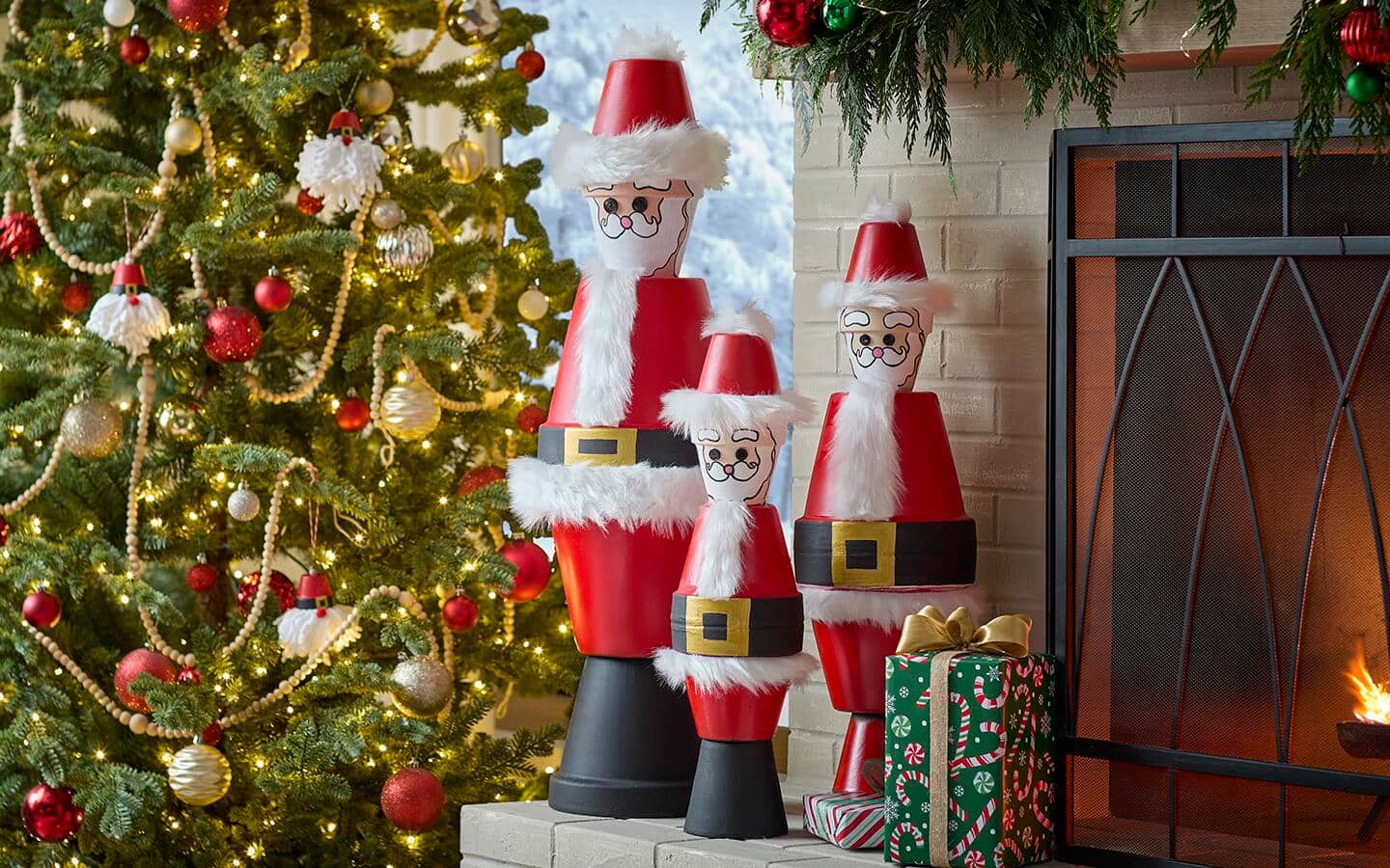 Three jolly Santas made from terra cotta pots and saucers standing in front of a fireplace.