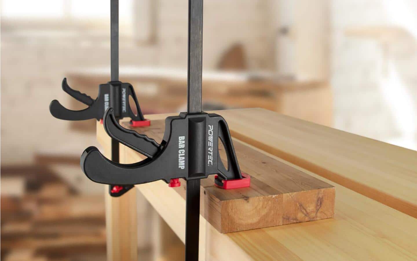 A red and black clamp holding boards glued together in place.
