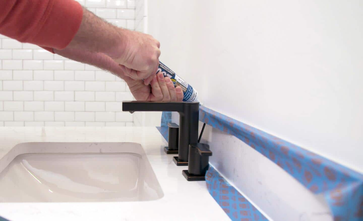 A person uses a caulk gun to apply caulk on a bathroom sink counter.