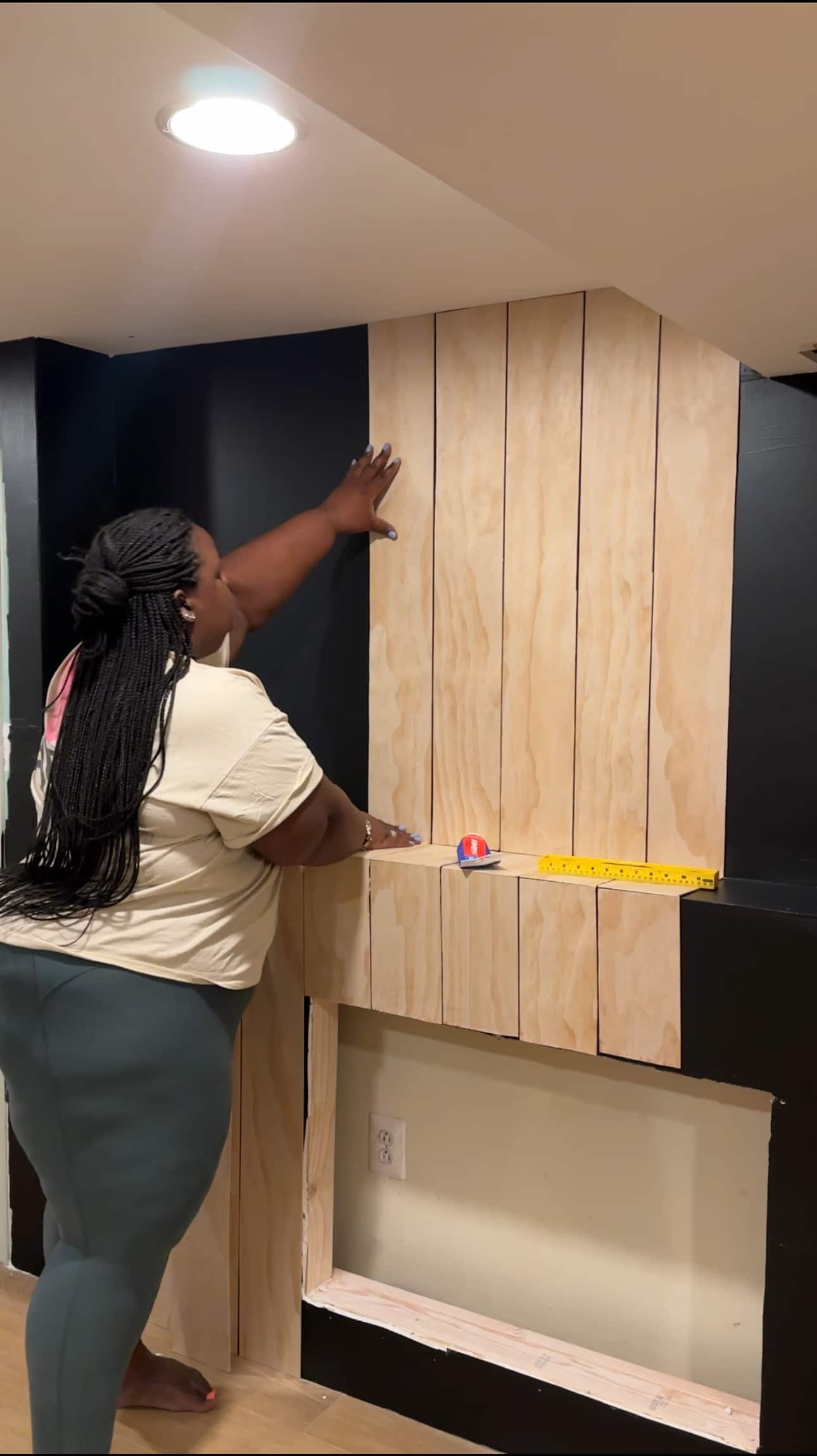 A woman installing planks vertically over a feature fireplace wall.
