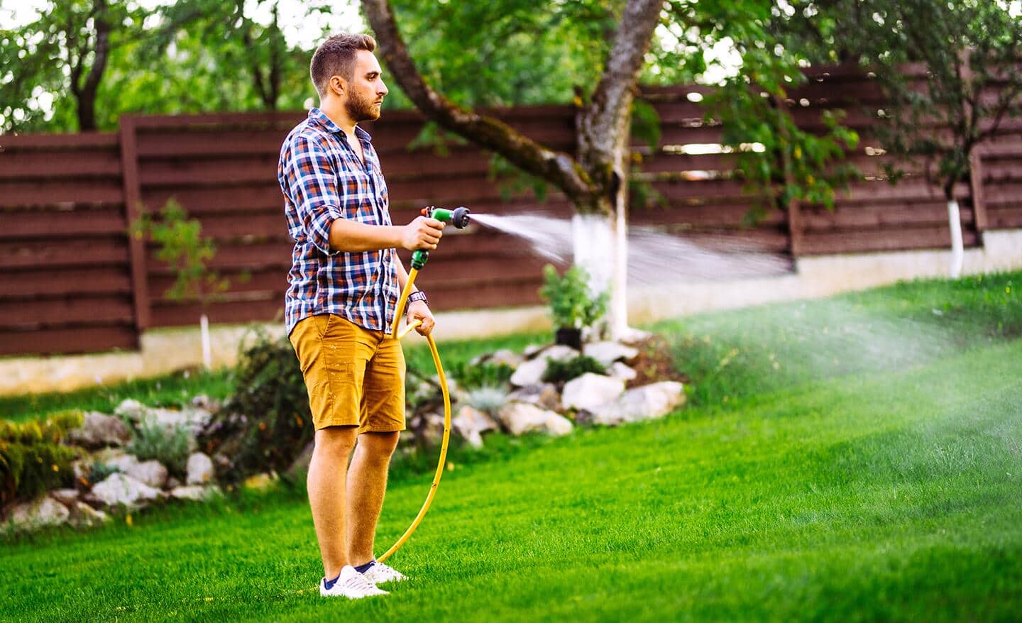 A person waters a lawn with a garden hose. A person waters a lawn with a garden hose.