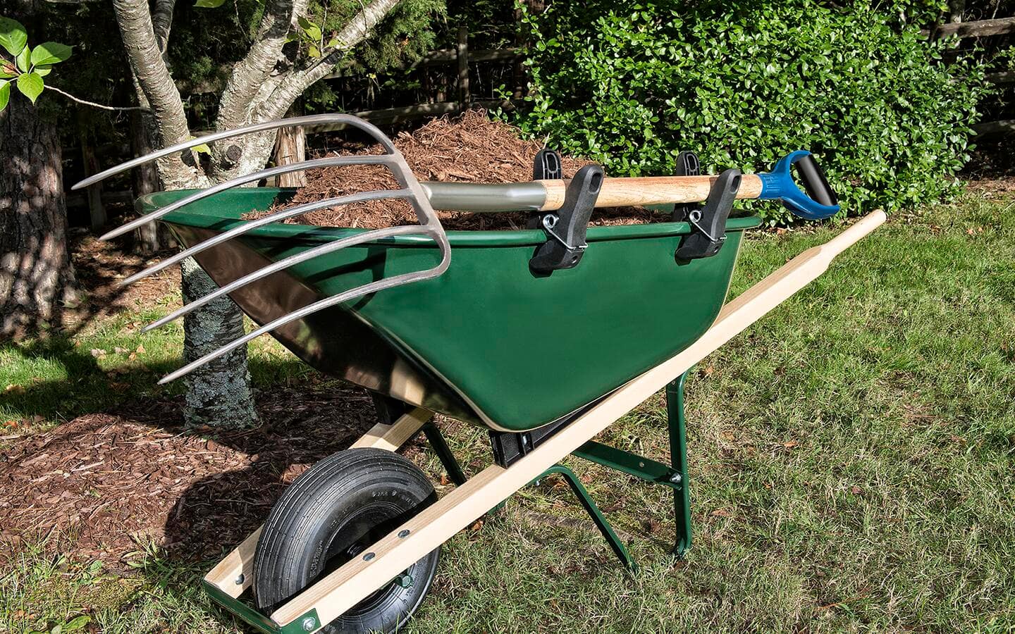 A wheelbarrow filled with a pitchfork and other tools for planting a tree. 