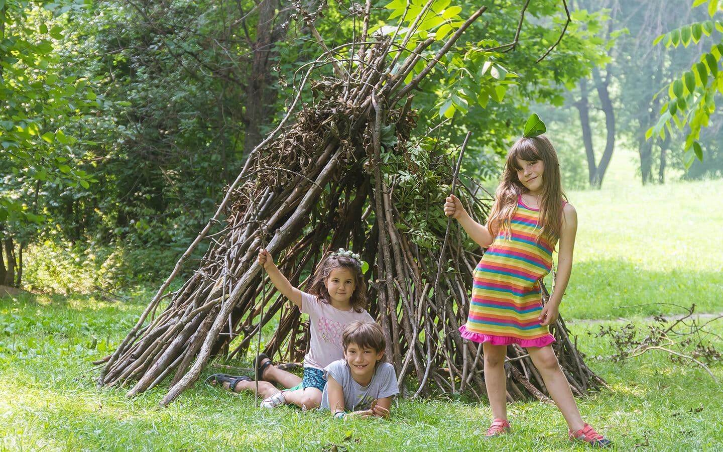 Three children play by a teepee made of sticks Three children play by a teepee made of sticks