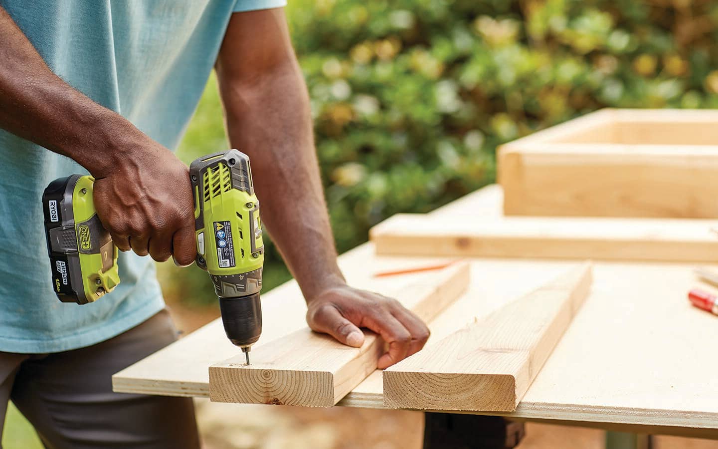 A person drills a pilot hole in the wedge of a cold frame.