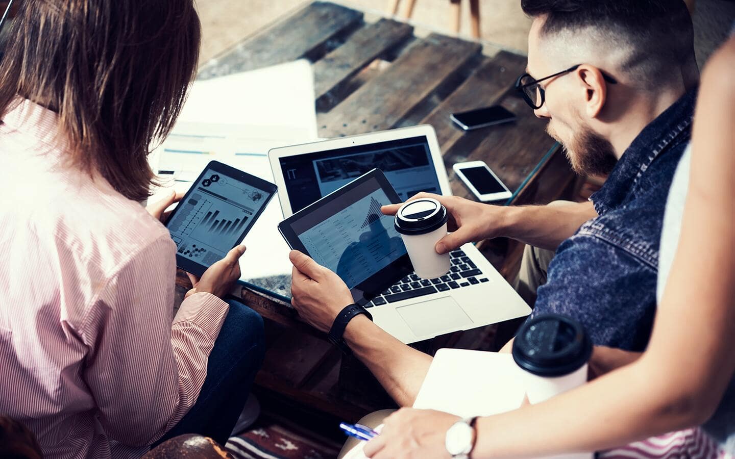 Two people use tablets to monitor their smart home devices, including a nearby laptop and smartphones. Two people use tablets to monitor their smart home devices, including a nearby laptop and smartphones.