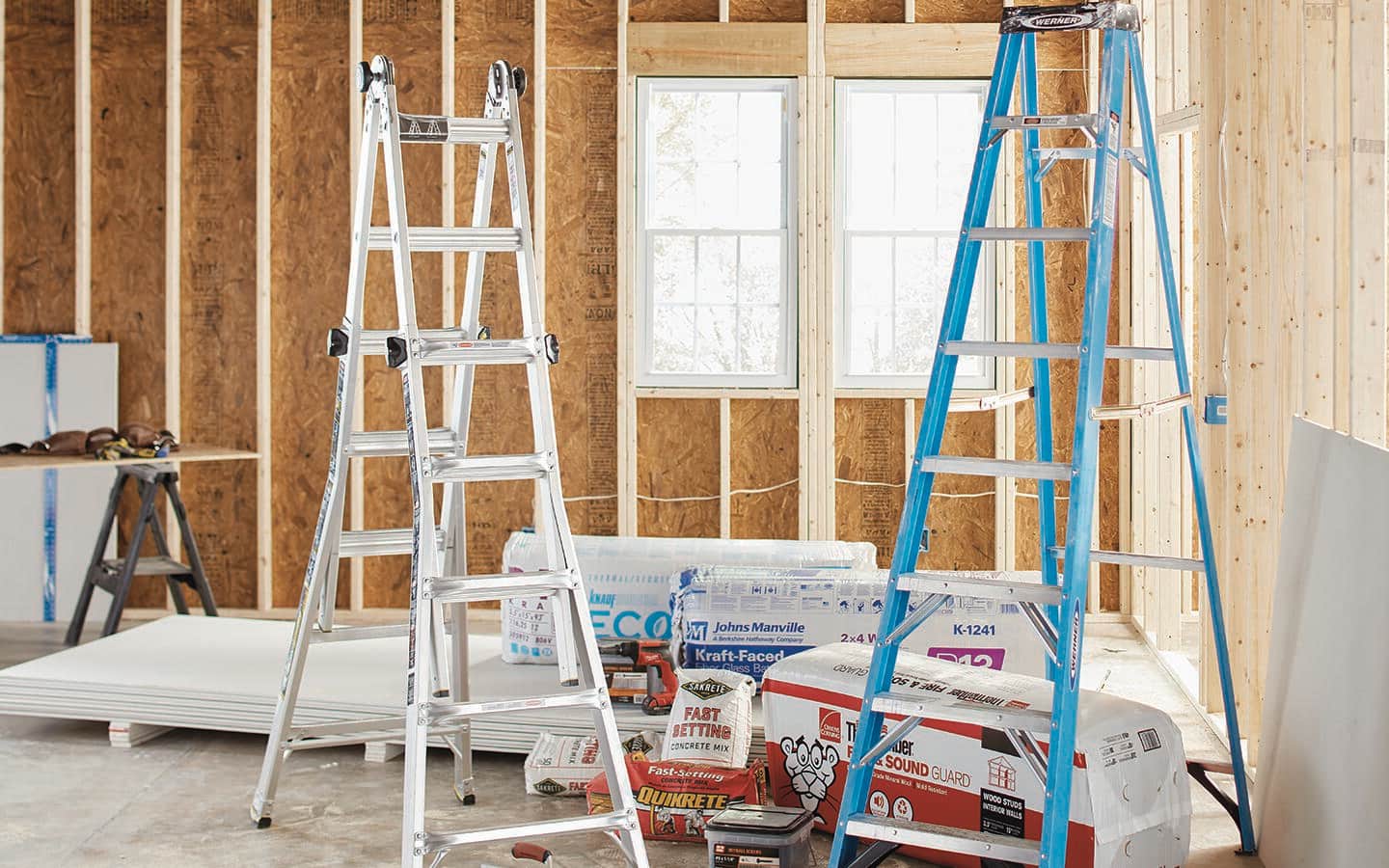 White and blue step ladders with other materials in an unfinished room.