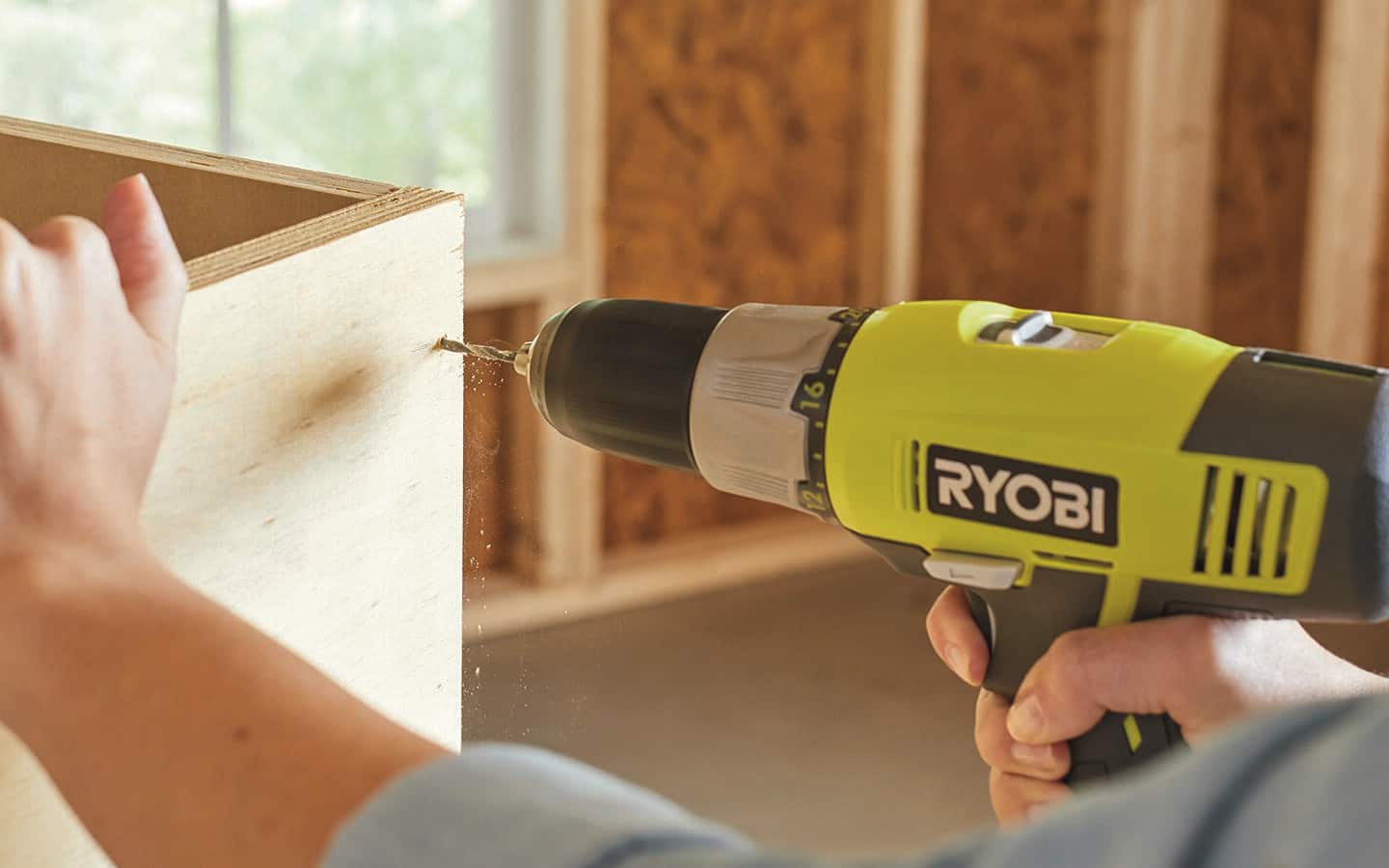 A person using a power drill to pre-drill holes in plywood. A person using a power drill to pre-drill holes in plywood.