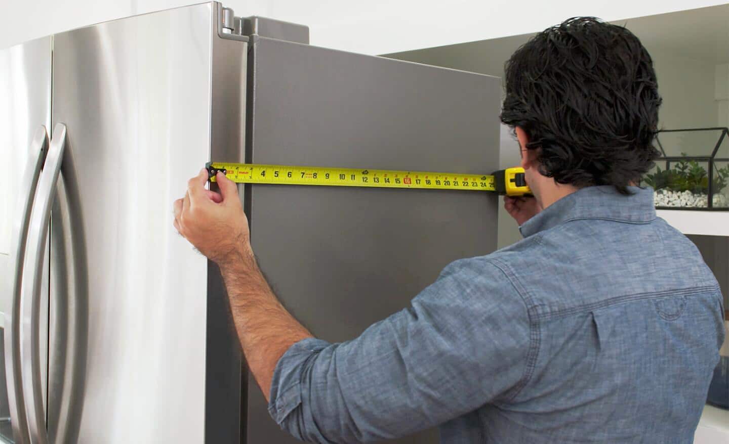 A person measuring the side of a refrigerator. 