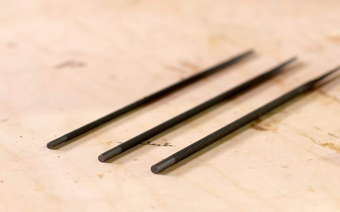 Three round metal files lay diagonally on a wood table. Three round metal files lay diagonally on a wood table.