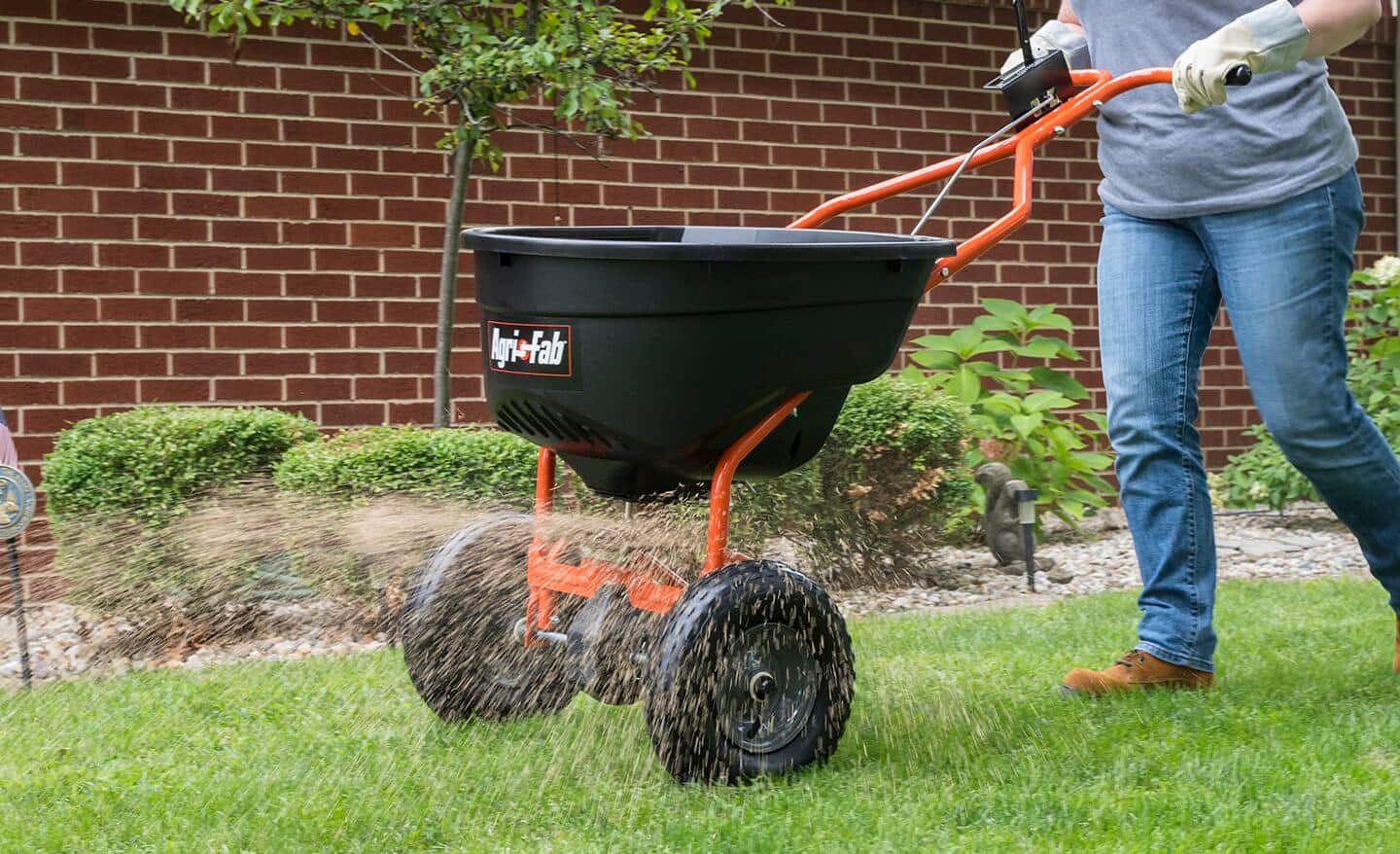 A person seeds a lawn with a spreader. A person seeds a lawn with a spreader.