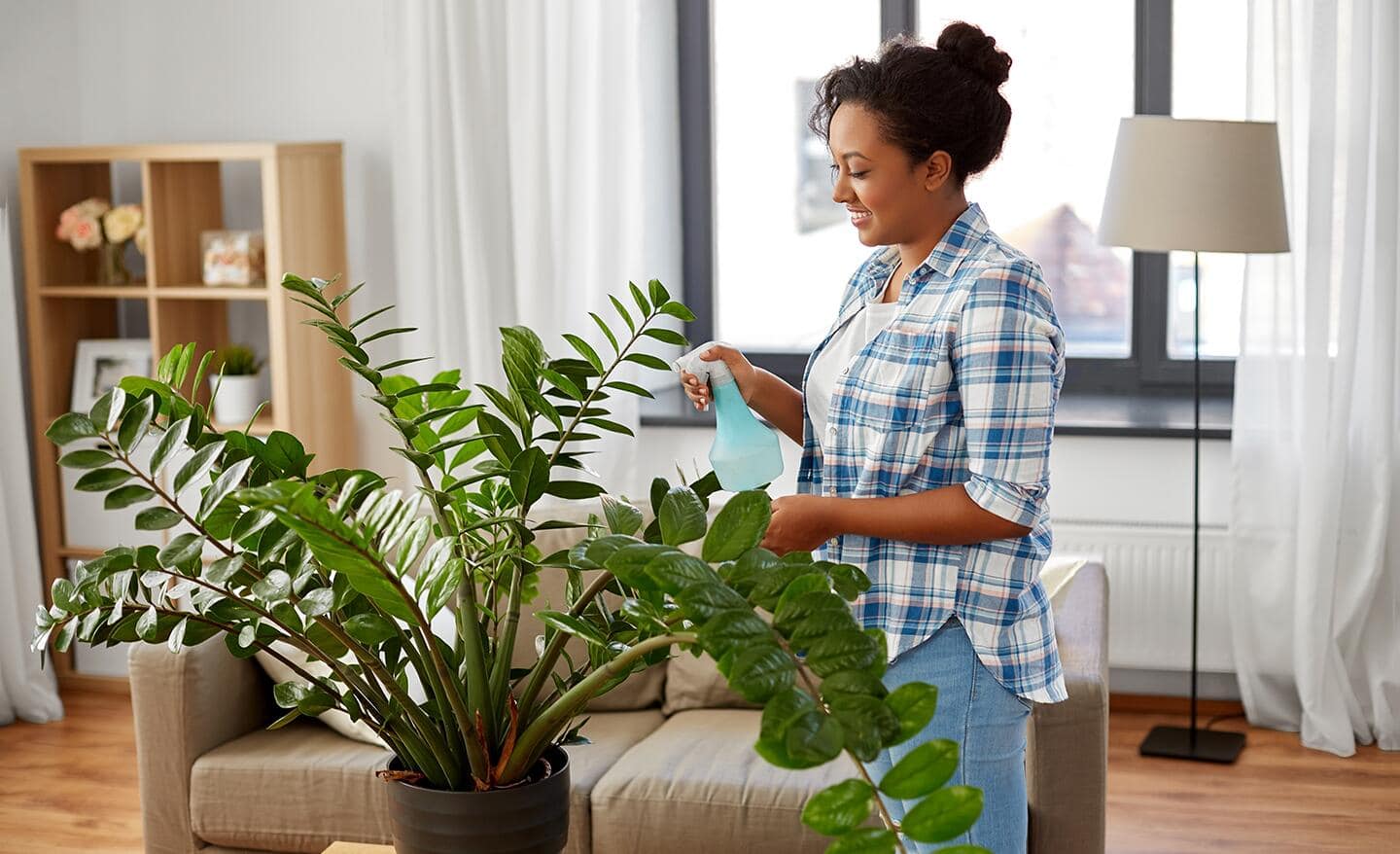 A woman uses a spray bottle to spritz a large houseplant.