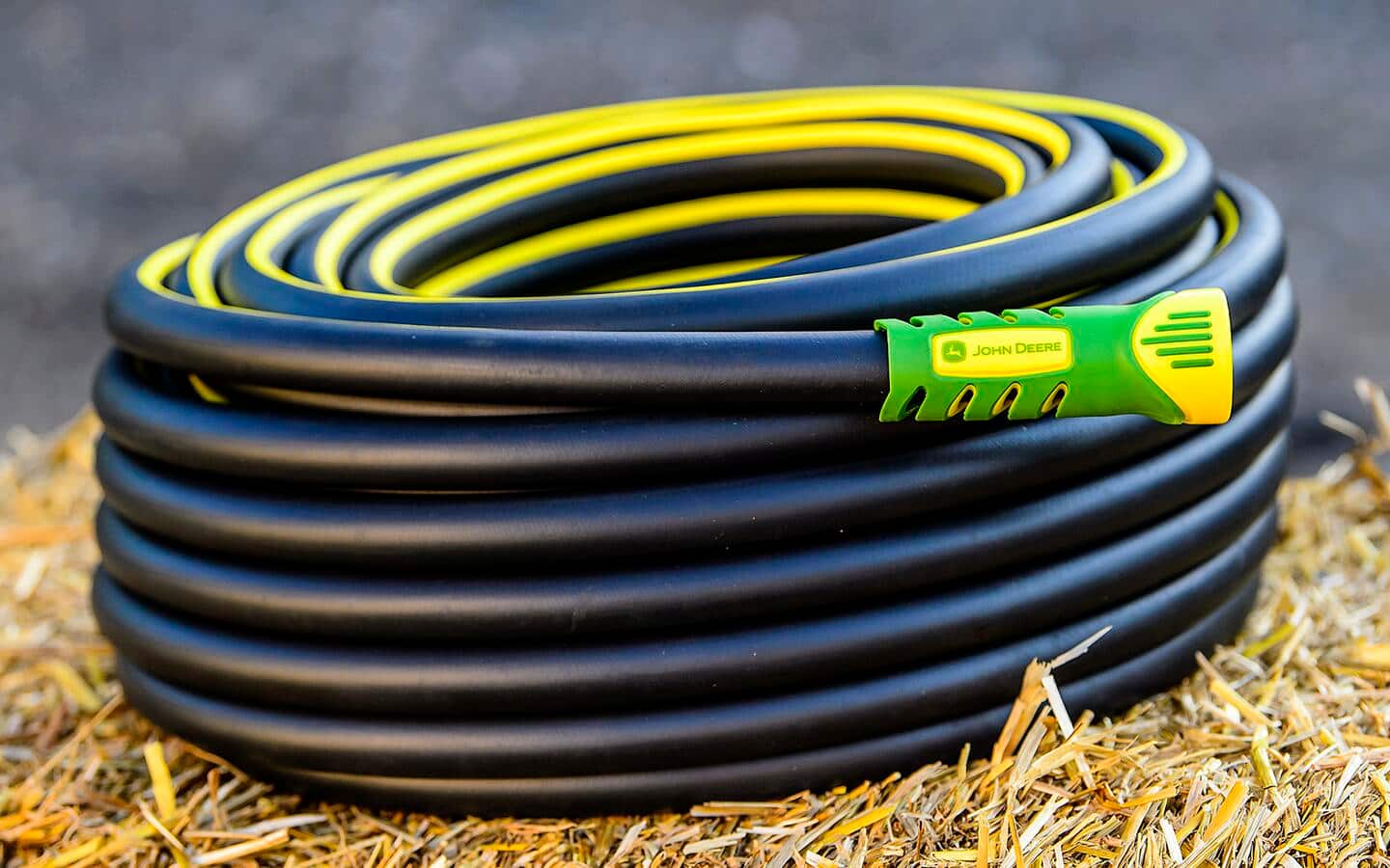 A yellow and black commercial-grade standard garden hose on dried grass.