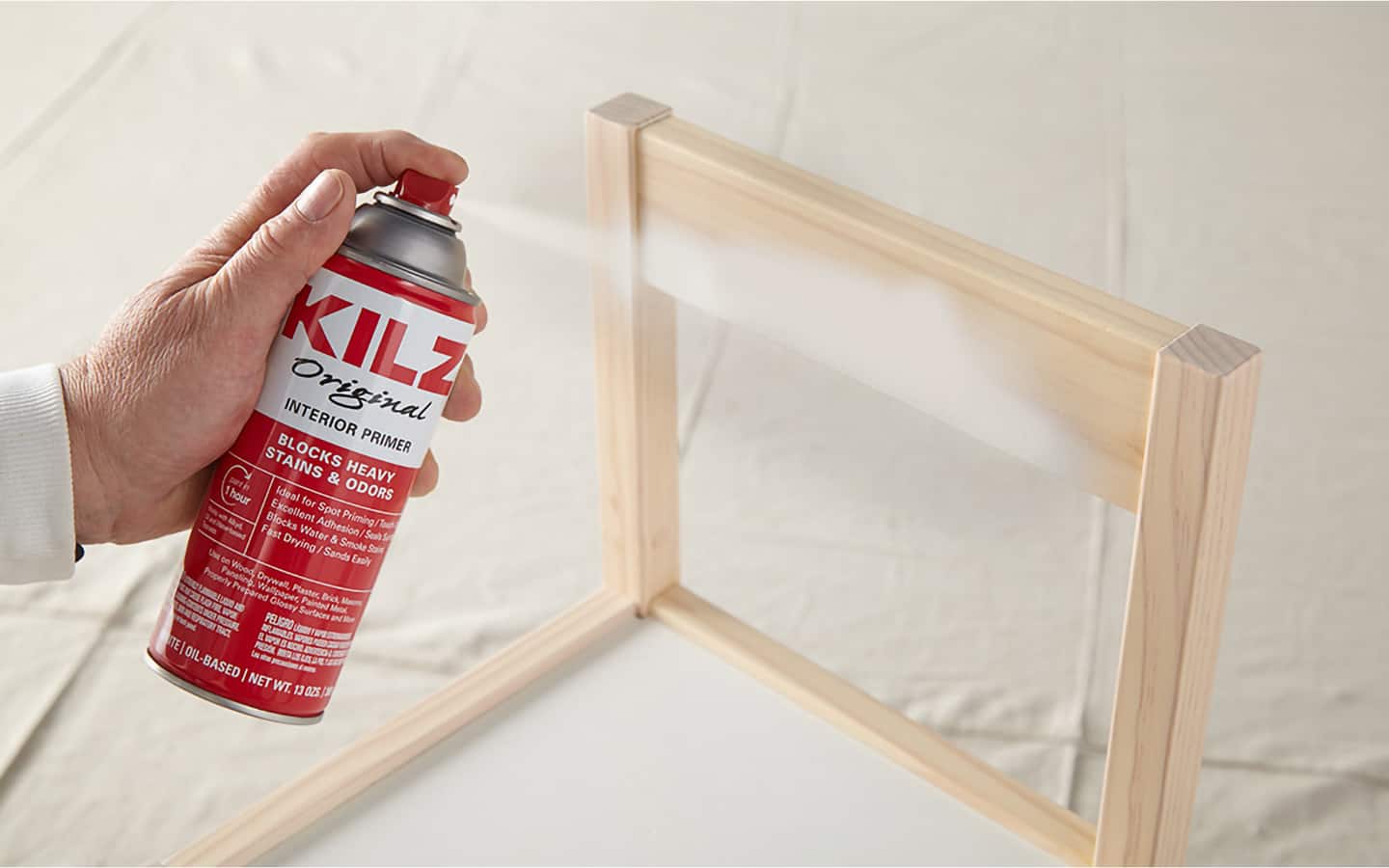 A person spraying a coat of primer paint onto a wood chair.