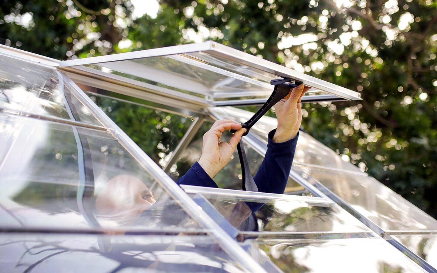 A person opens a vent panel on a greenhouse