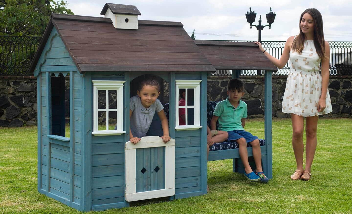 Children inside a blue, wood playhouse with a brown roof in a park.