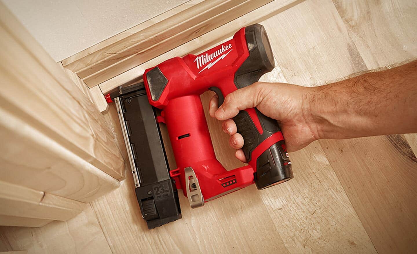 A person uses a cordless pin nailer on a baseboard project.