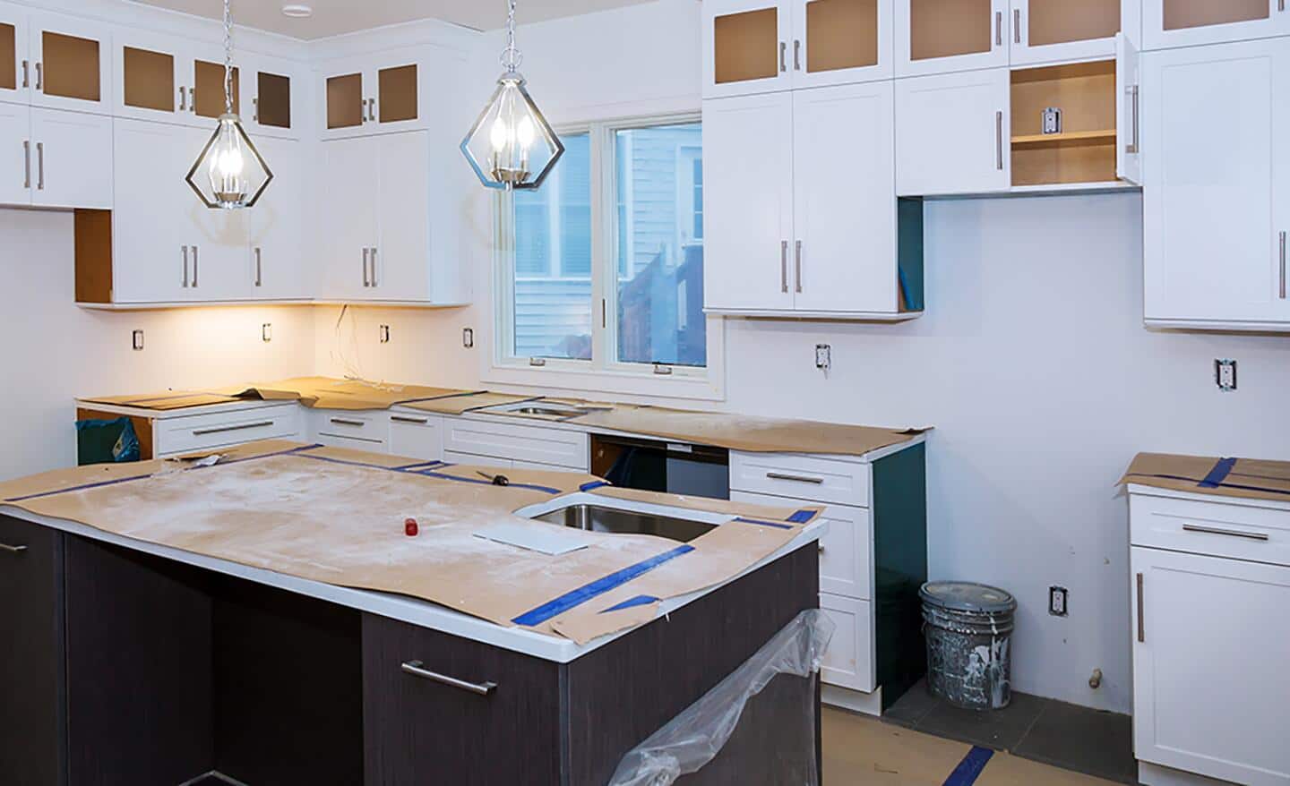 A kitchen with partially-installed cabinets and a large space where a refrigerator will be installed.
