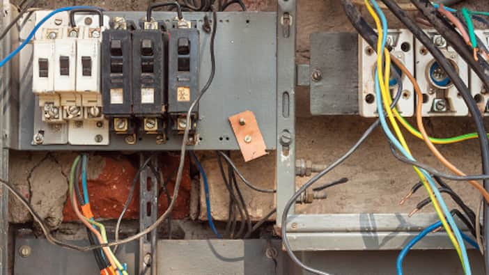 An old house has multiple wires attached to a breaker panel.