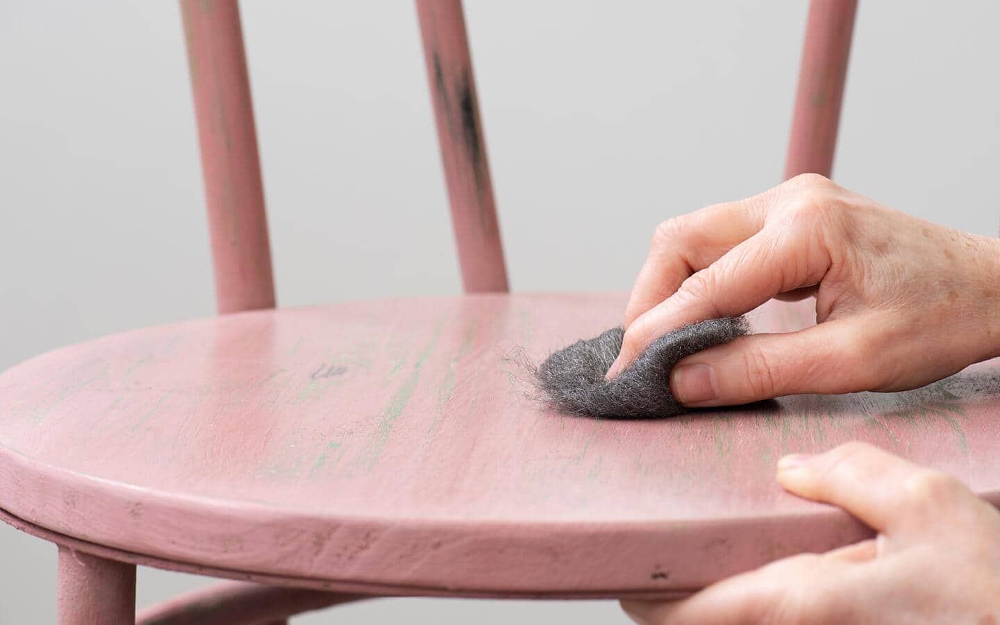 Someone uses steel wool on a painted stool.