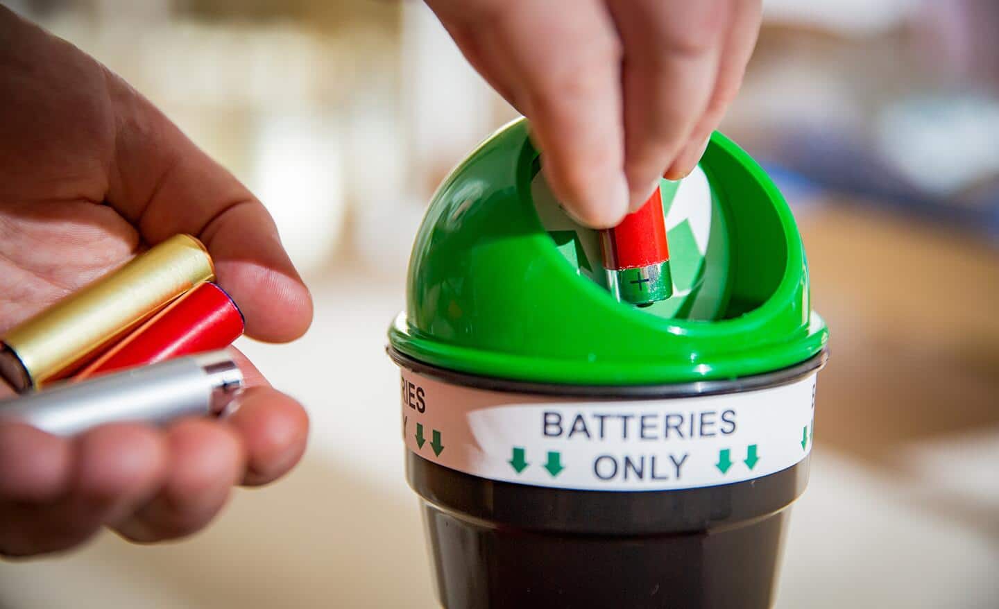 A person puts batteries into a tiny recycling container.