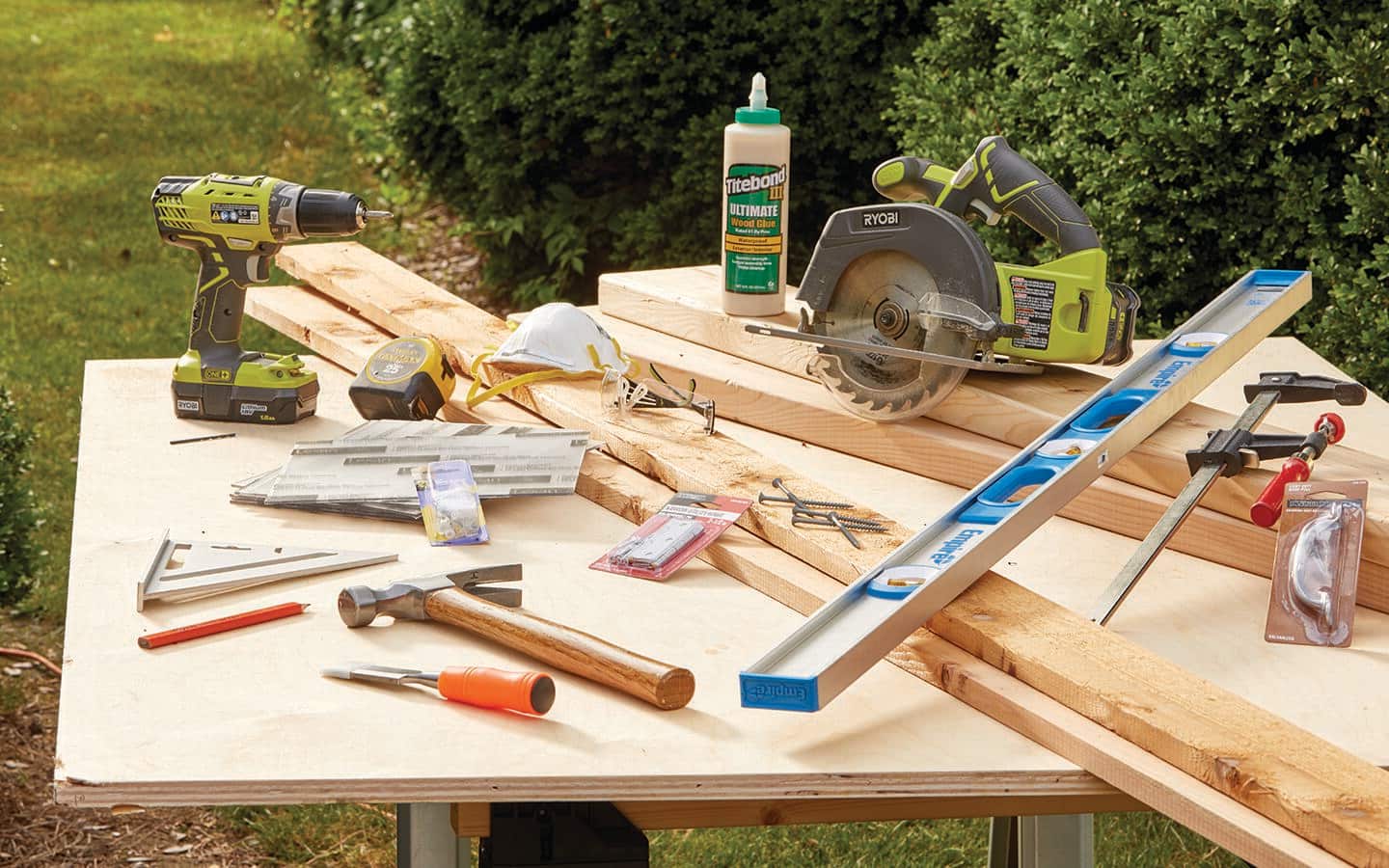 A worktable displays the tools and materials needed to make a cold frame, including a hammer, a level, a drill and a circular saw.
