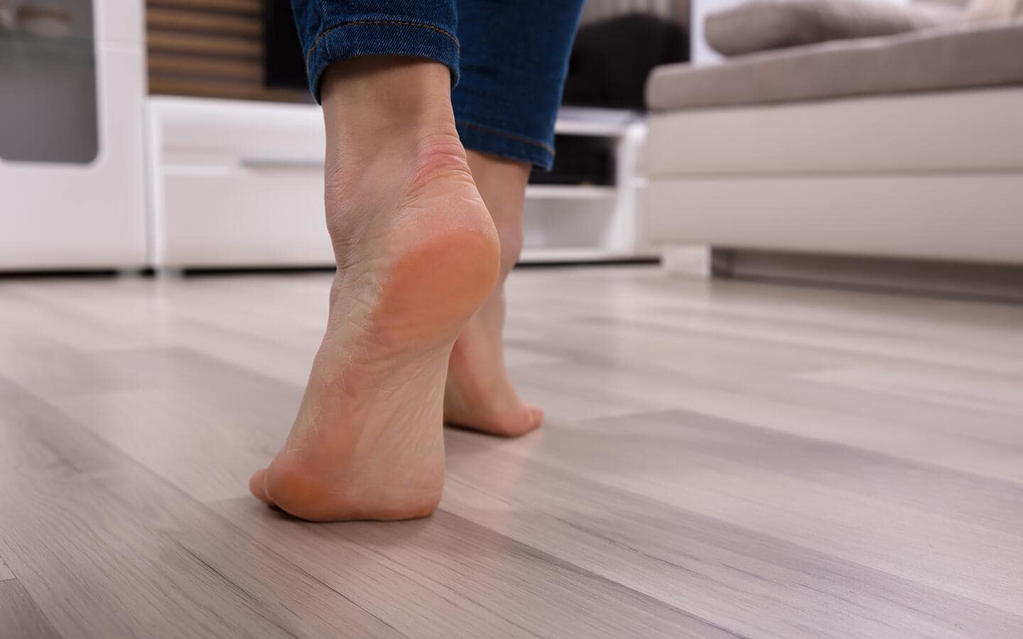 A barefoot person walking on beige hardwood flooring.