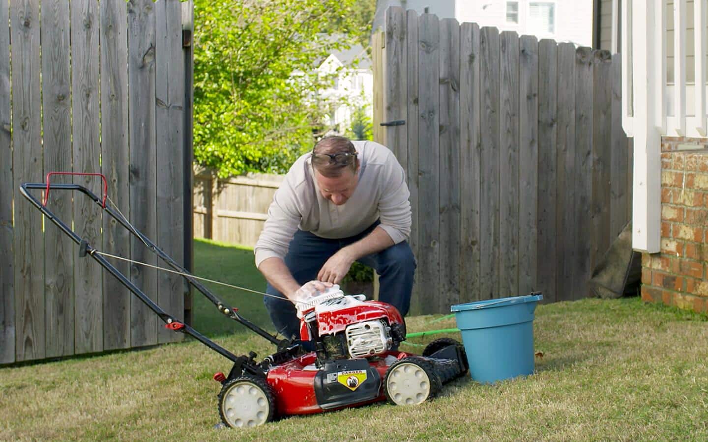 A person cleans the outside of a lawn mower with a sudsy brush. A person cleans the outside of a lawn mower with a sudsy brush.