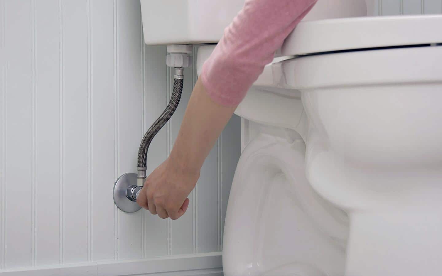 A person disconnecting the water supply behind a toilet. A person disconnecting the water supply behind a toilet.