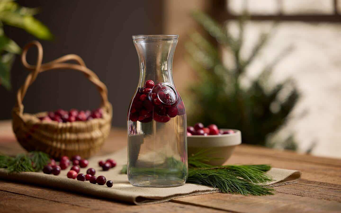 Fresh cranberries floating in a clear glass vase of water with a basket and a bowl of fresh cranberries on a table Fresh cranberries floating in a clear glass vase of water with a basket and a bowl of fresh cranberries on a table