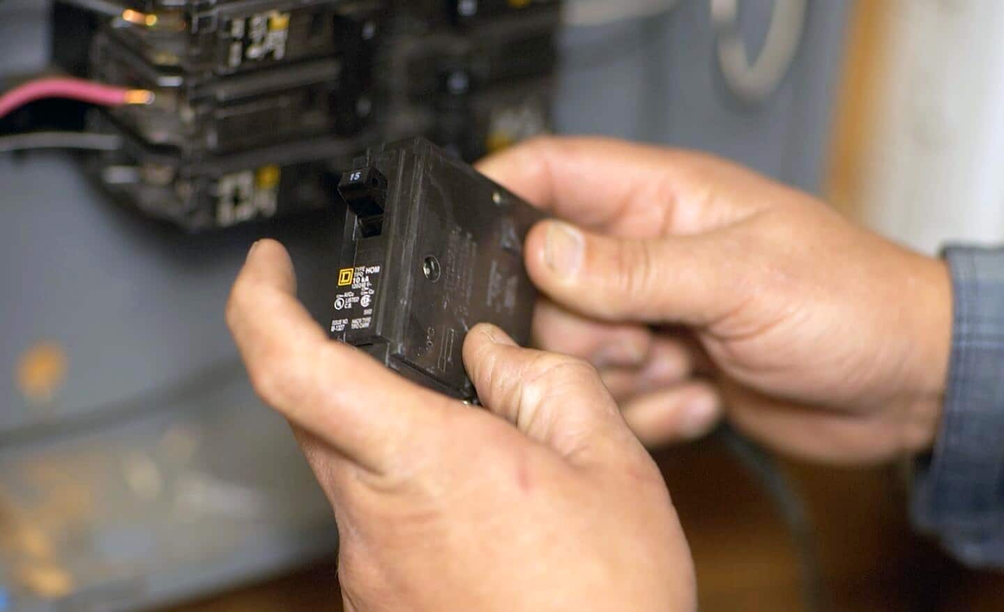 A person replacing a circuit breaker in an electrical panel.