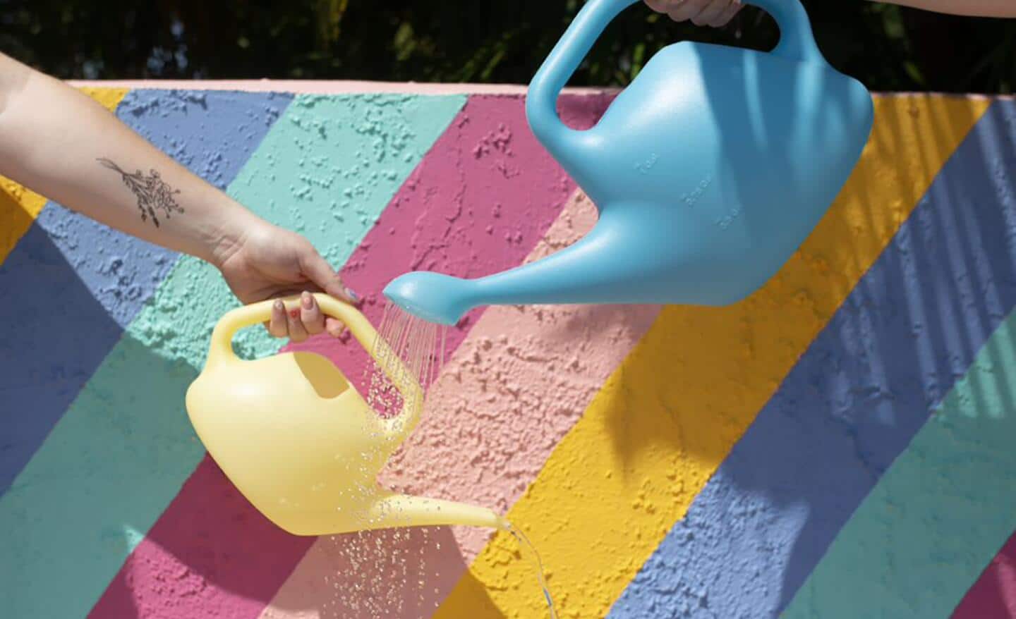 A yellow and a green watering can against a colorful wall