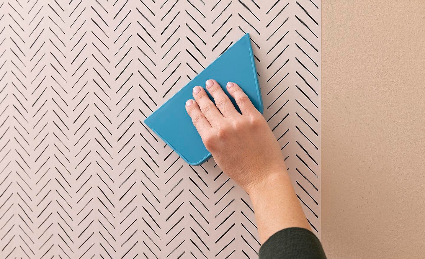 Someone installing wallpaper with a blue plastic smoother.