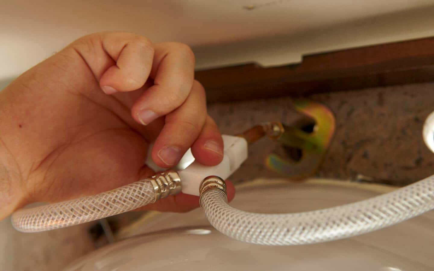 A person attaching hot and cold faucet supply tubes by hand. A person attaching hot and cold faucet supply tubes by hand.