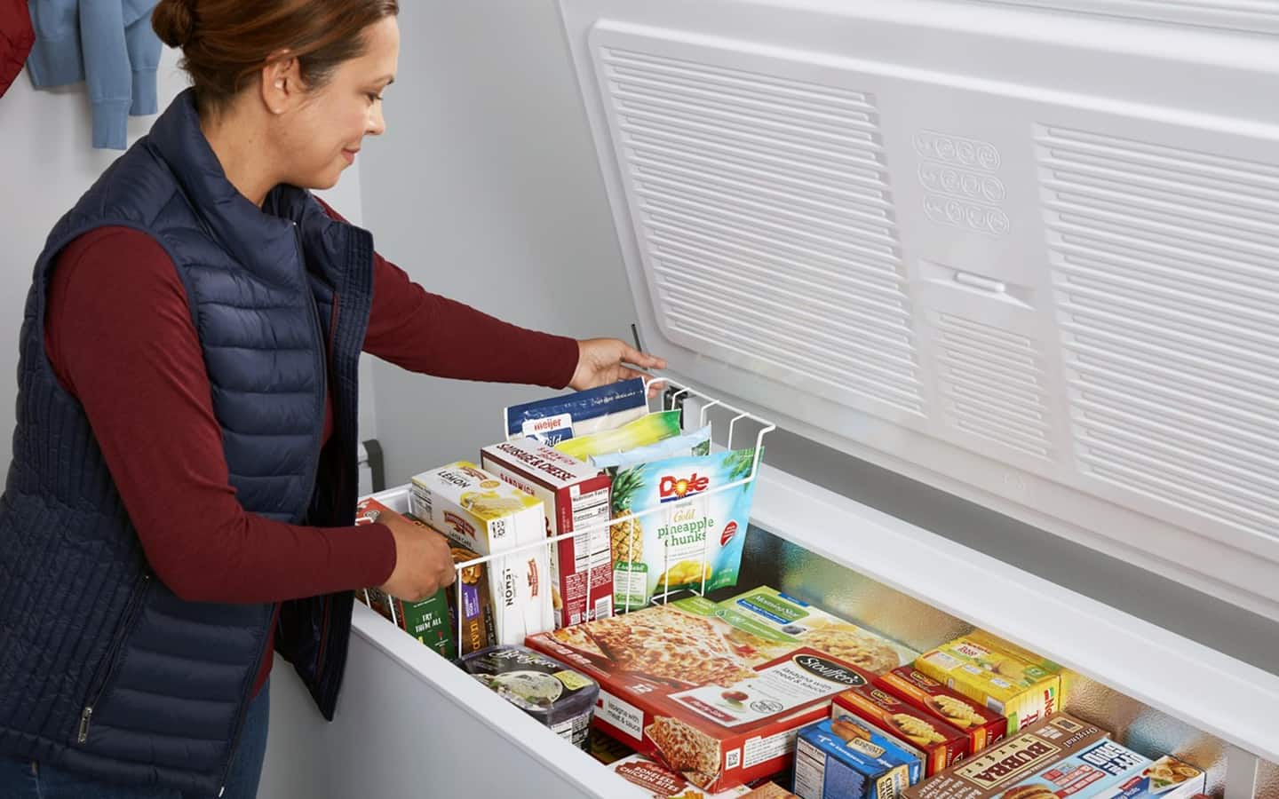 Someone places frozen items into a wire bin inside an open chest freezer. 