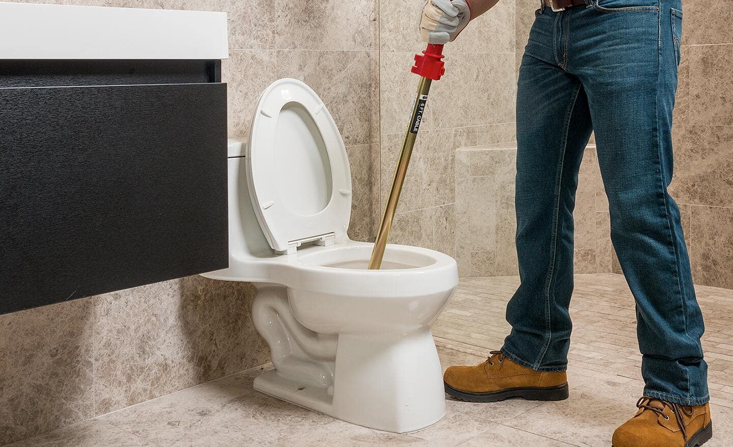 A person uses a plumbing snake to unclog a toilet.