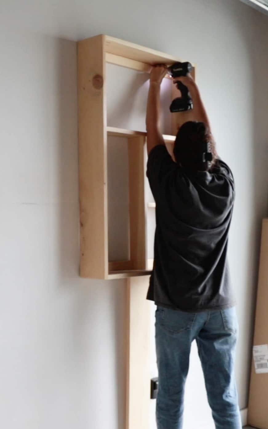 A person hanging the cabinet to the wall.