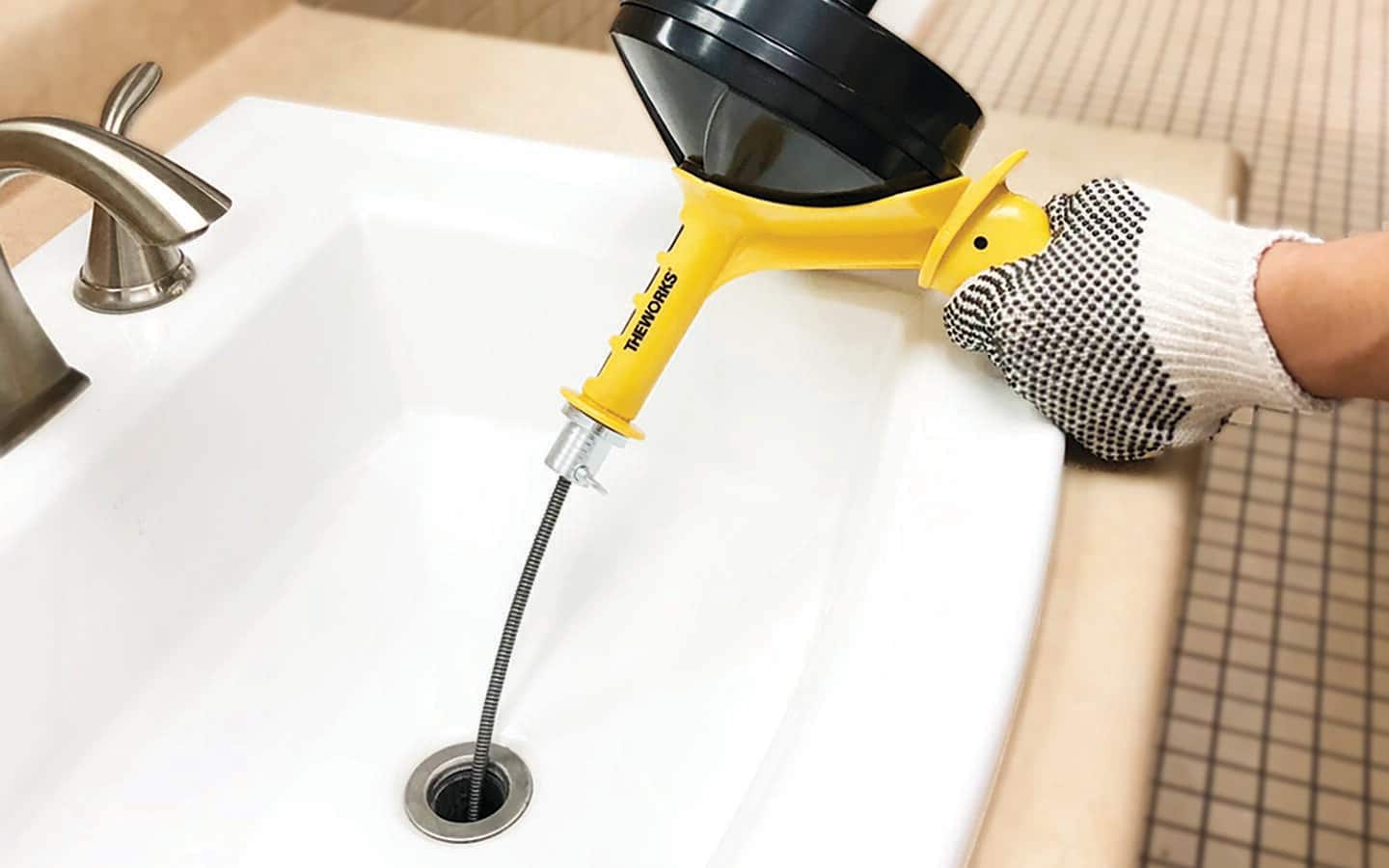 A person uses an auger in a bathroom sink. A person uses an auger in a bathroom sink.