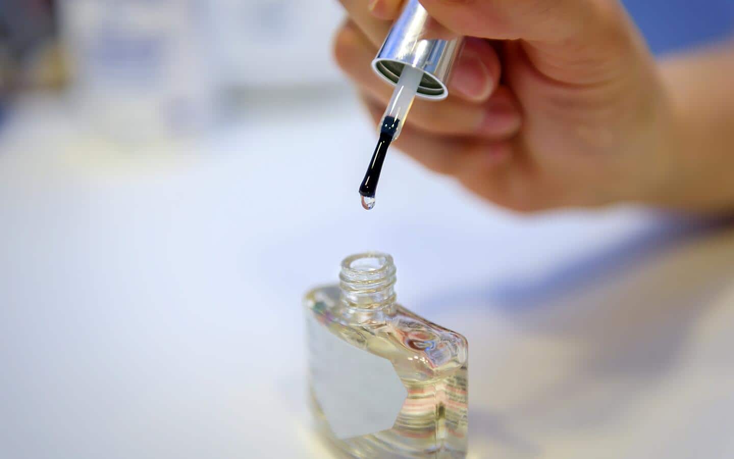An applicator brush being dipped into a bottle of clear nail polish.