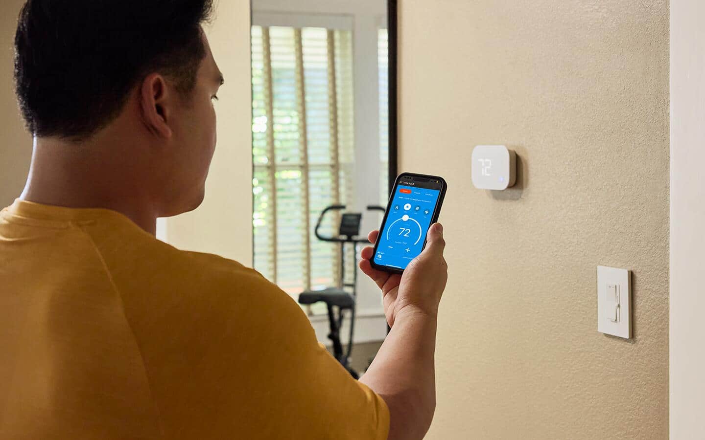 An individual using a smartphone to program their smart thermostat.